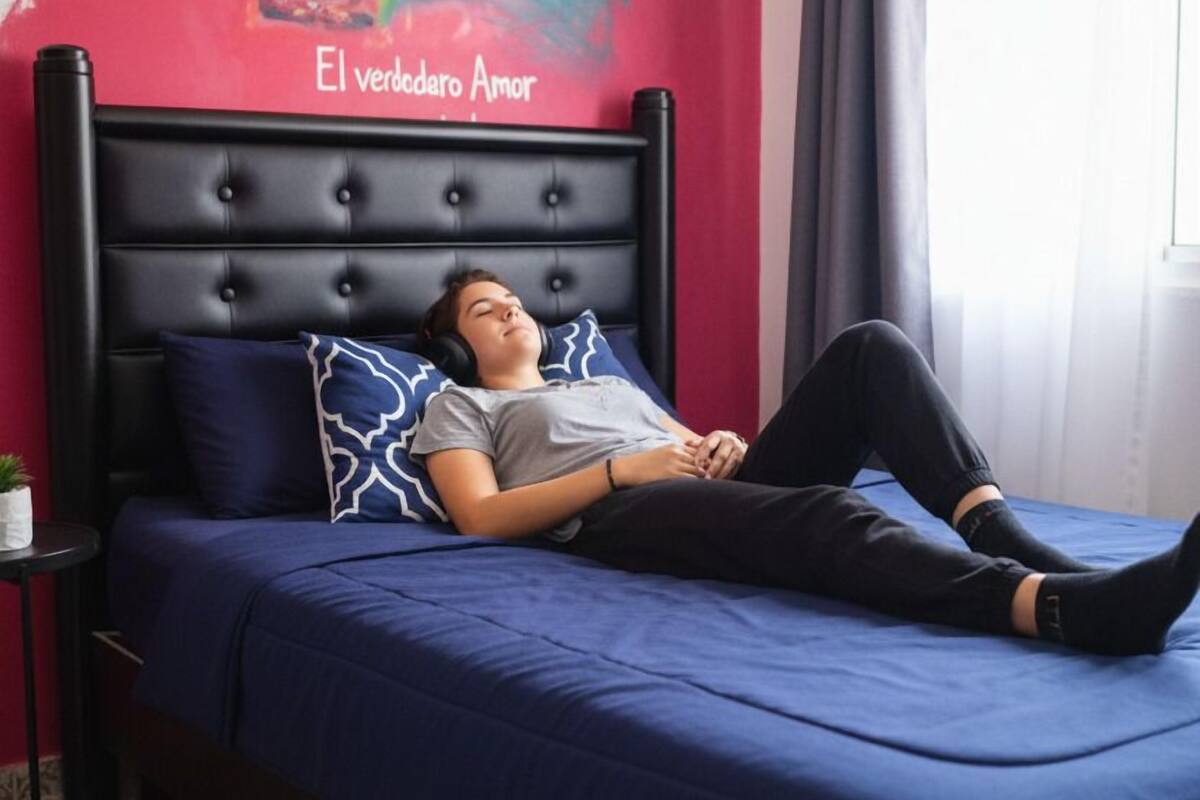 A person lying on a bed in a room with a red wall and a mural.