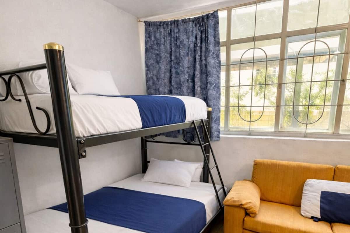 A bunk bed with white and blue bedding, a yellow sofa, and a window with curtains.