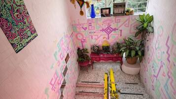 Una escalera con patrones geométricos coloridos en las paredes y un pequeño altar con plantas y un cartel que dice 'BRAVE'.