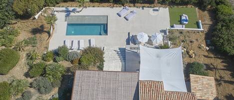 An aerial view of a property with a swimming pool, lounge chairs, and a covered patio area.