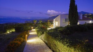Ein modernes Haus mit einem Kiesweg, der zum Eingang führt, umgeben von gepflegten Hecken und einer hohen Zypresse.