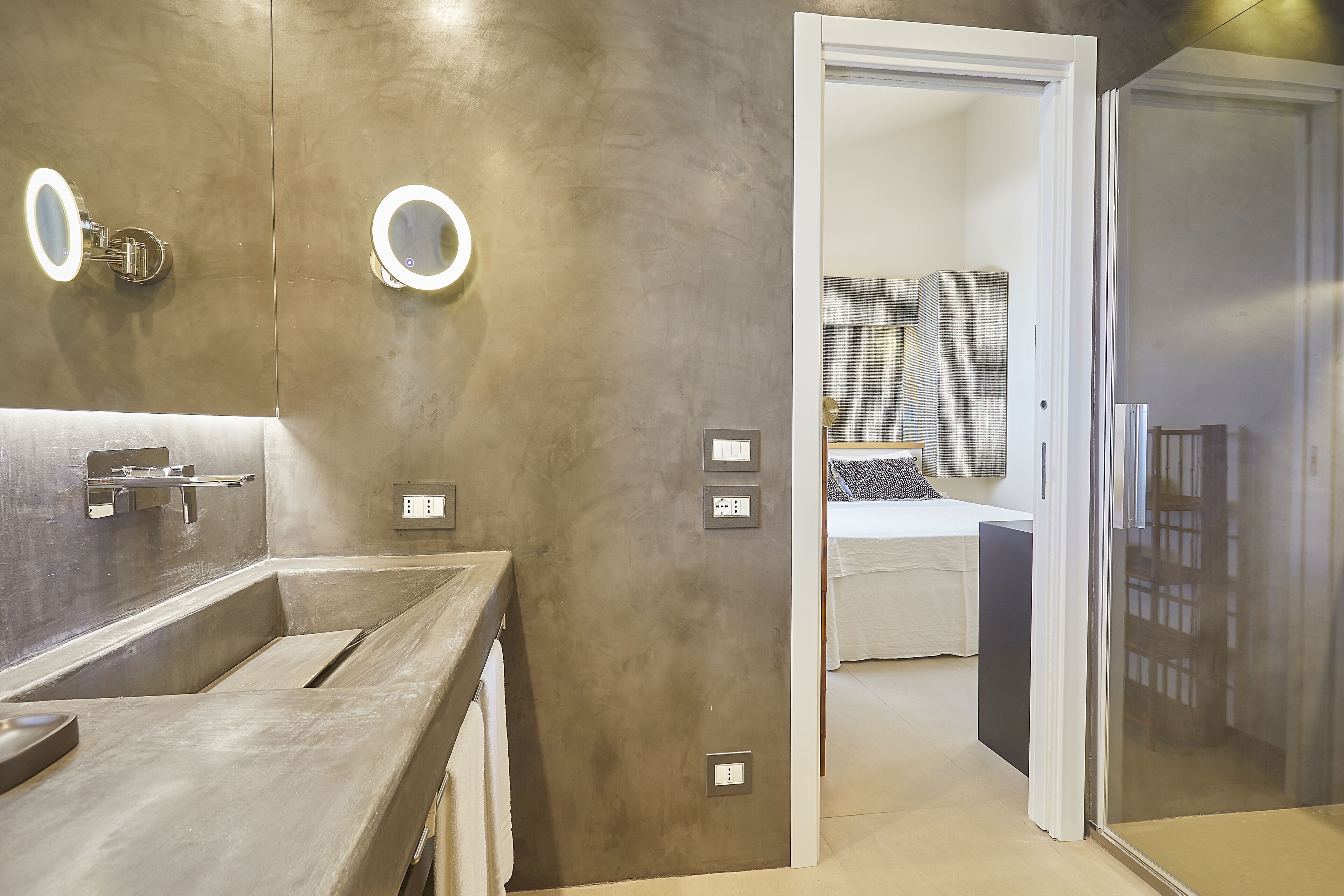 A modern bathroom with a large sink, two illuminated mirrors, and a shower area.