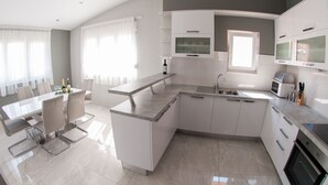 A modern kitchen with a central island, built-in appliances, and a dining area with a table and chairs. - Apartments Anita - Luxury Three-Bedroom Apartment with Terrace (Stobrec)