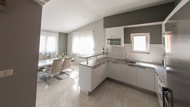 A modern kitchen with white cabinets, a dining area with a glass table, and a large window with curtains. - Apartments Anita - Luxury Three-Bedroom Apartment with Terrace (Stobrec)