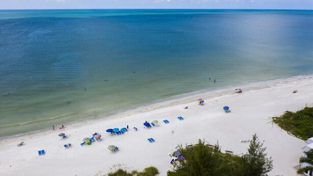 A beach with clear turquoise water, white sand, and several beach umbrellas and lounge chairs. - Holmes Beach | Couples Gulf Coast Retreat | Pool + Beach (Holmes Beach)