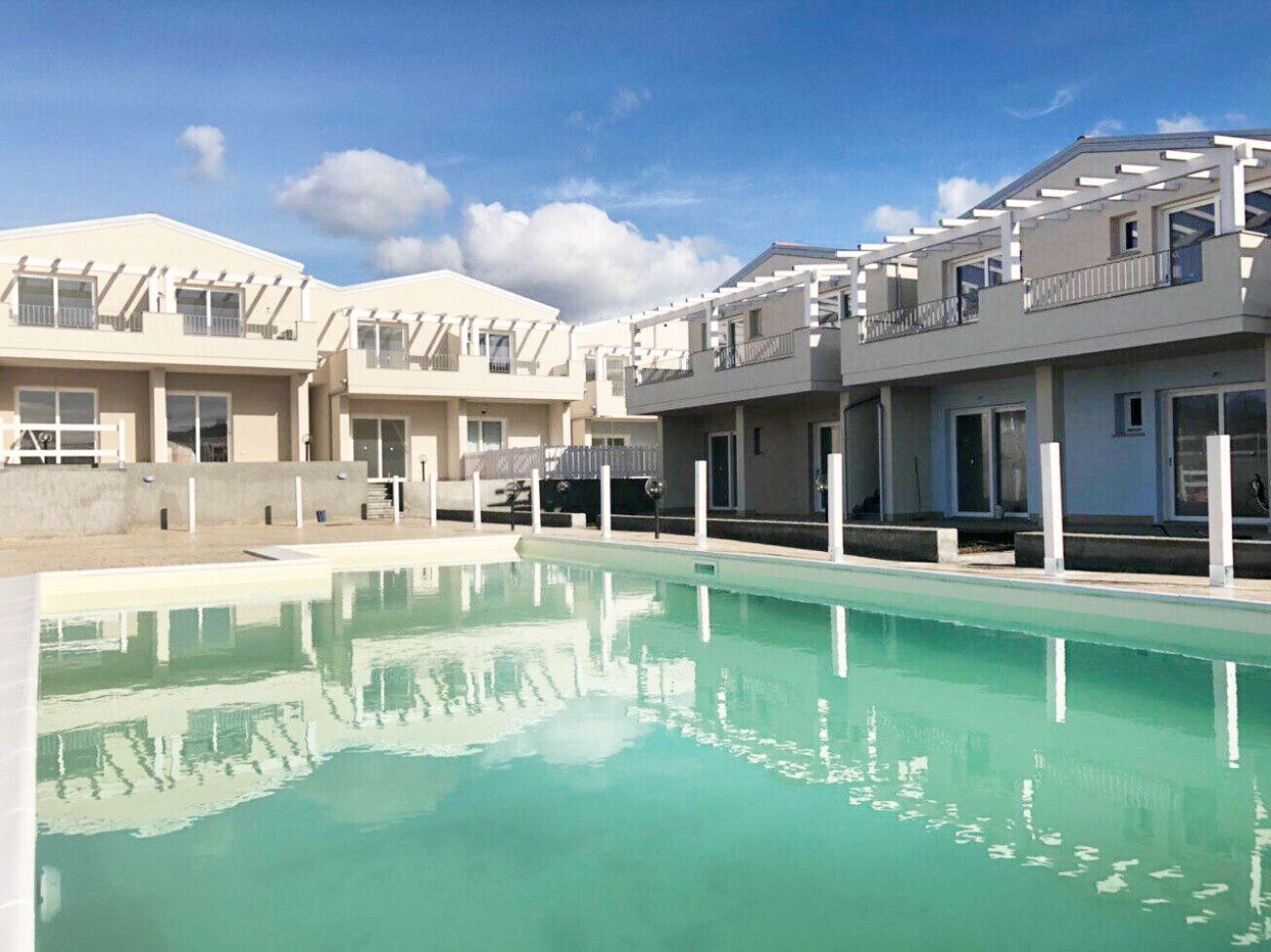 A modern residential building with a swimming pool, balconies, and a clear blue sky.