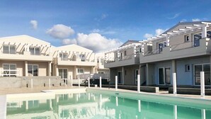 Un moderno edificio residencial con piscina, balcones y un cielo azul despejado.