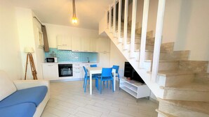 Una cocina moderna con armarios blancos, un comedor con sillas azules y una escalera con barandas blancas.