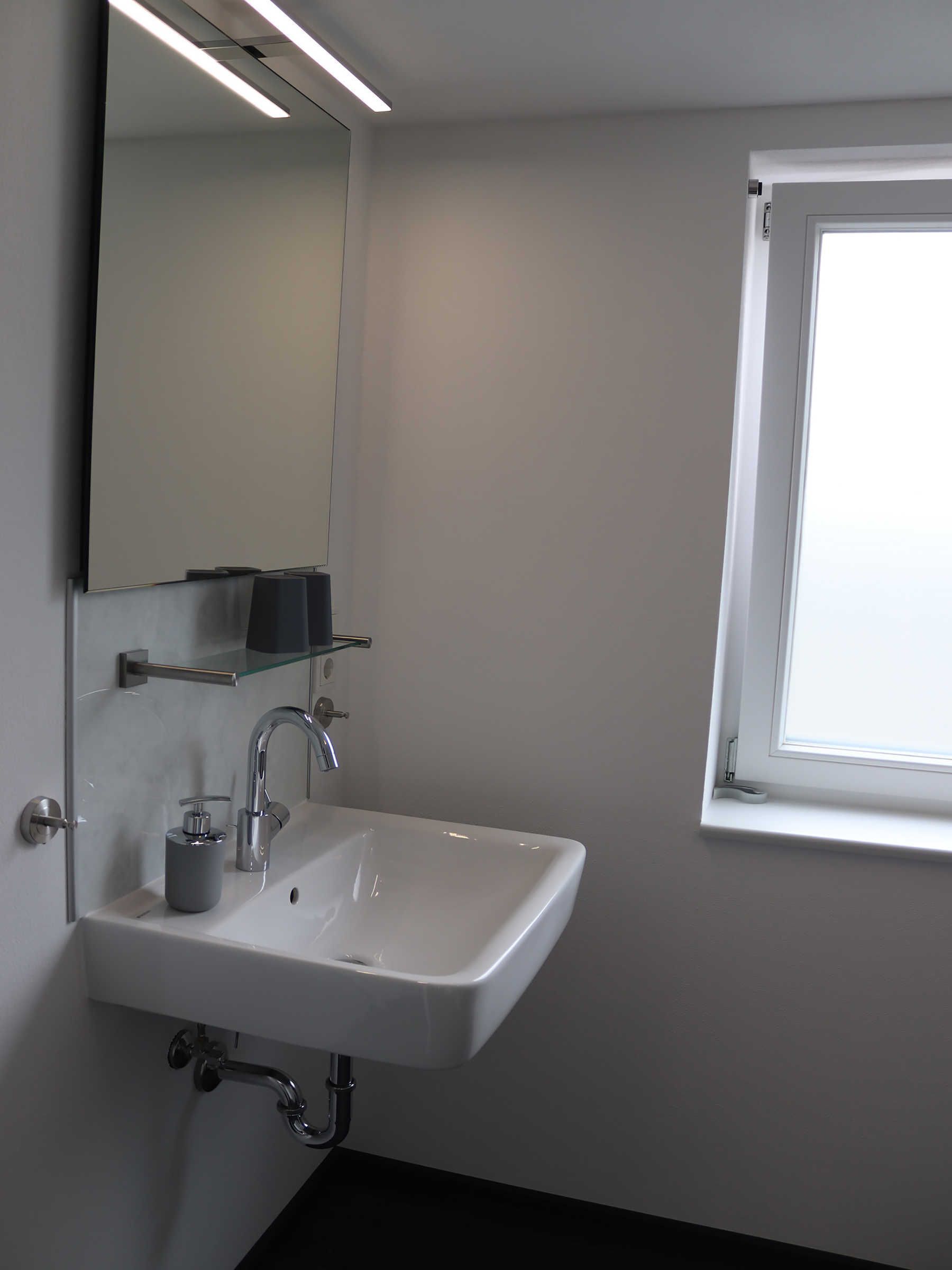 A modern bathroom with a white sink, a mirror, and a window.