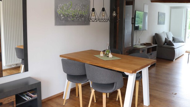 A modern dining area with a wooden table, grey upholstered chairs, and a pendant light fixture.