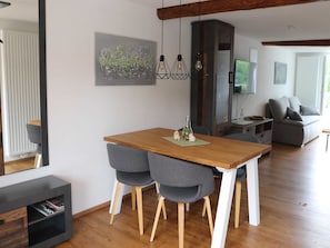 A modern dining area with a wooden table, grey upholstered chairs, and a pendant light fixture. - Eder-Ufer 1 Vacation Apartment - Eder-Ufer Vacation Apartments (Edertal)