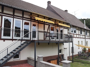 Un bâtiment à deux étages doté d’un balcon, d’un escalier et d’un espace extérieur aménagé pour s’asseoir.