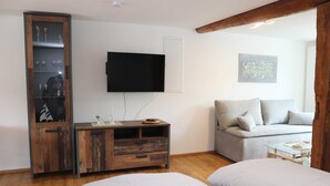 A modern room with a wooden cabinet, a flat-screen TV, a sofa, and two beds with striped bedding. - Vacation apartment Eder-Ufer 1 - Holiday apartments Eder-Ufer (Edertal)
