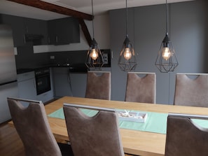 Un espace repas moderne avec une table en bois, six chaises et des luminaires suspendus.