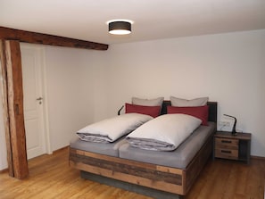 Une chambre à coucher avec un lit en bois, deux oreillers, une table de chevet et une commode.
