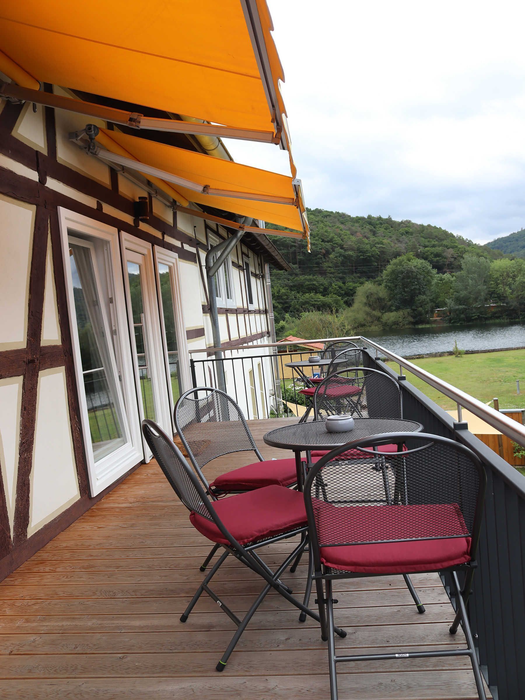 Un pontile in legno con posti a sedere all'aperto, vista su un lago e un edificio con un balcone.