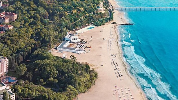 An aerial view of a coastal area with a beach, a pier, and a building complex with multiple structures.