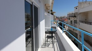 A balcony with a table and chairs, a glass door, and a blue railing. - Happy Days Home Apartment and Studio (Rhodes)