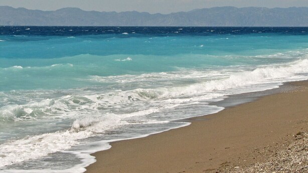 A beach with waves crashing onto the shore and mountains in the background. - Happy Days Home Apartment and Studio (Rhodes)
