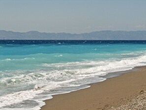 A beach with waves crashing onto the shore and mountains in the background. - Happy Days Home Apartment and Studio (Rhodes)
