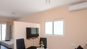 A modern living room with a sofa, a dining table with chairs, a TV, and a bed. - Happy Days Home Apartment and Studio (Rhodes)