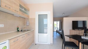 A modern kitchen with wooden cabinets, a built-in sink, and a dining area with a black table and chairs. - Happy Days Home Apartment and Studio (Rhodes)