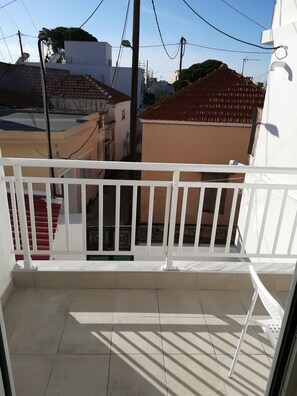 A balcony with a white railing, tiled floor, and a view of neighboring buildings. - Happy Days Home Apartment and Studio (Rhodes)