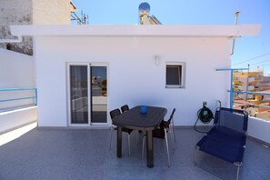 A rooftop terrace with a table and chairs, a sliding glass door, a small window, and a blue folding chair. - Happy Days Home Apartment and Studio (Rhodes)