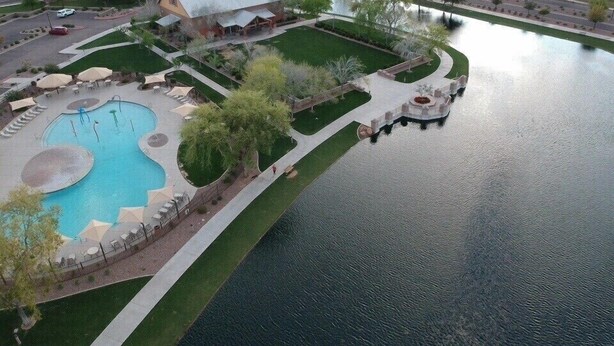 An aerial view of a residential area with a swimming pool, a gazebo, and a small bridge over a water body. - Modern Remodel + Amenities Galore! (Gilbert)