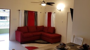 A living room with a red sectional sofa, a dining table with a bowl and cup, and a ceiling fan. - Stylish 3BR House in Ocho Rios w/AC, Pool & Gym (Ocho Rios)