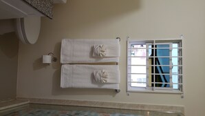 A bathroom with two towels hanging on a rack, a toilet, a window with a view, and a tiled floor. - Stylish 3BR House in Ocho Rios w/AC, Pool & Gym (Ocho Rios)