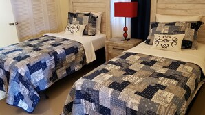 Two twin beds with matching quilts, a wooden nightstand with a lamp, and a wooden headboard. - Stylish 3BR House in Ocho Rios w/AC, Pool & Gym (Ocho Rios)
