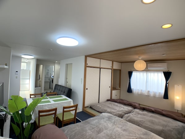 A room with a dining table, chairs, a sofa, a bed, and a ceiling light.
