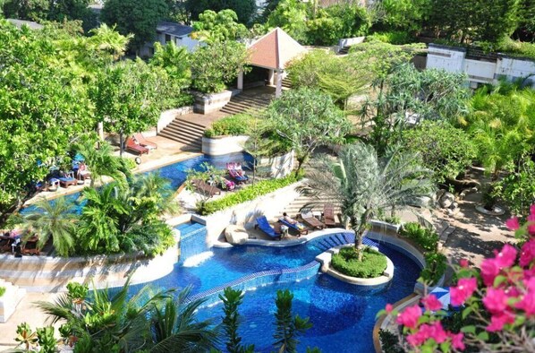 Relax by the resort's central pool surrounded by lush greenery and palm trees.