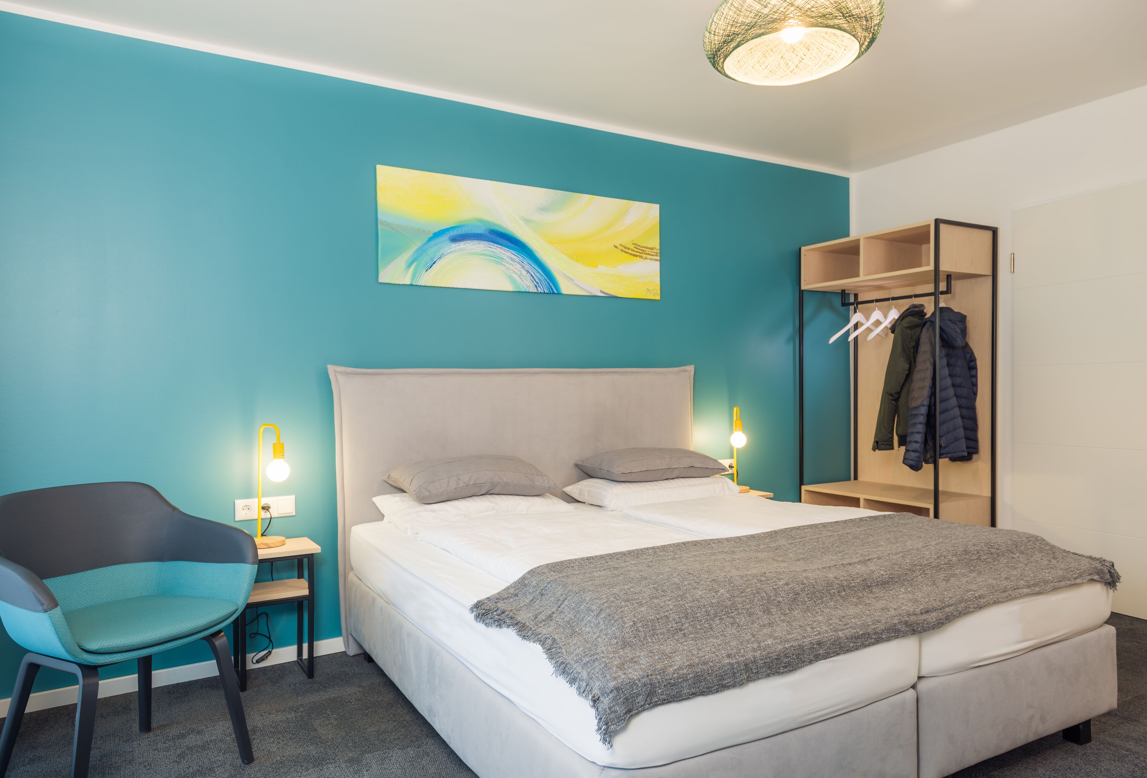 Um quarto moderno com uma cama, uma cadeira, uma mesa de cabeceira, um abajur e um cabideiro.