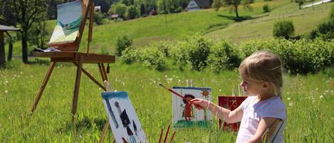 A child painting in a grassy field with a landscape in the background.