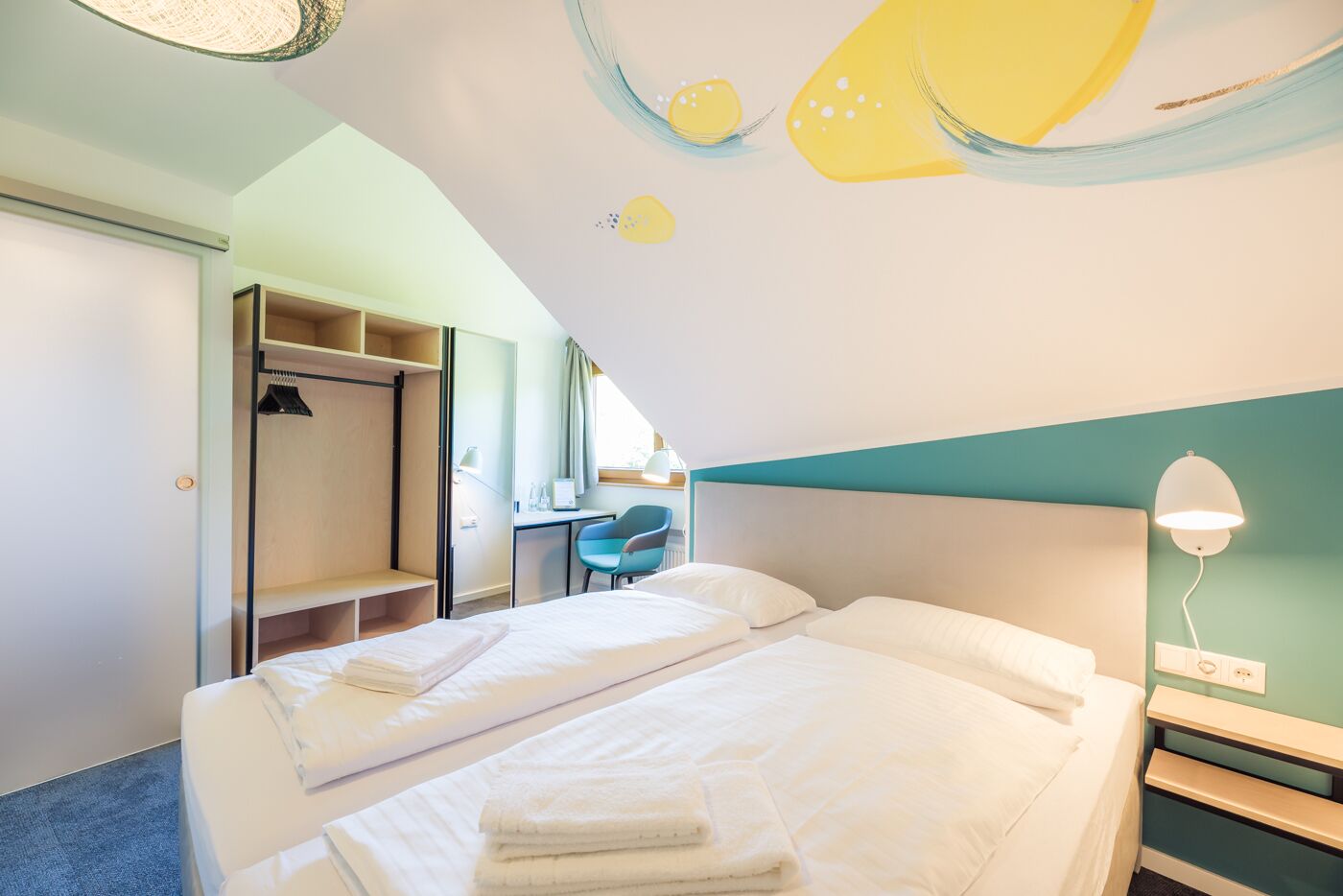 Une chambre d’hôtel avec deux lits, un bureau, une chaise et une armoire.