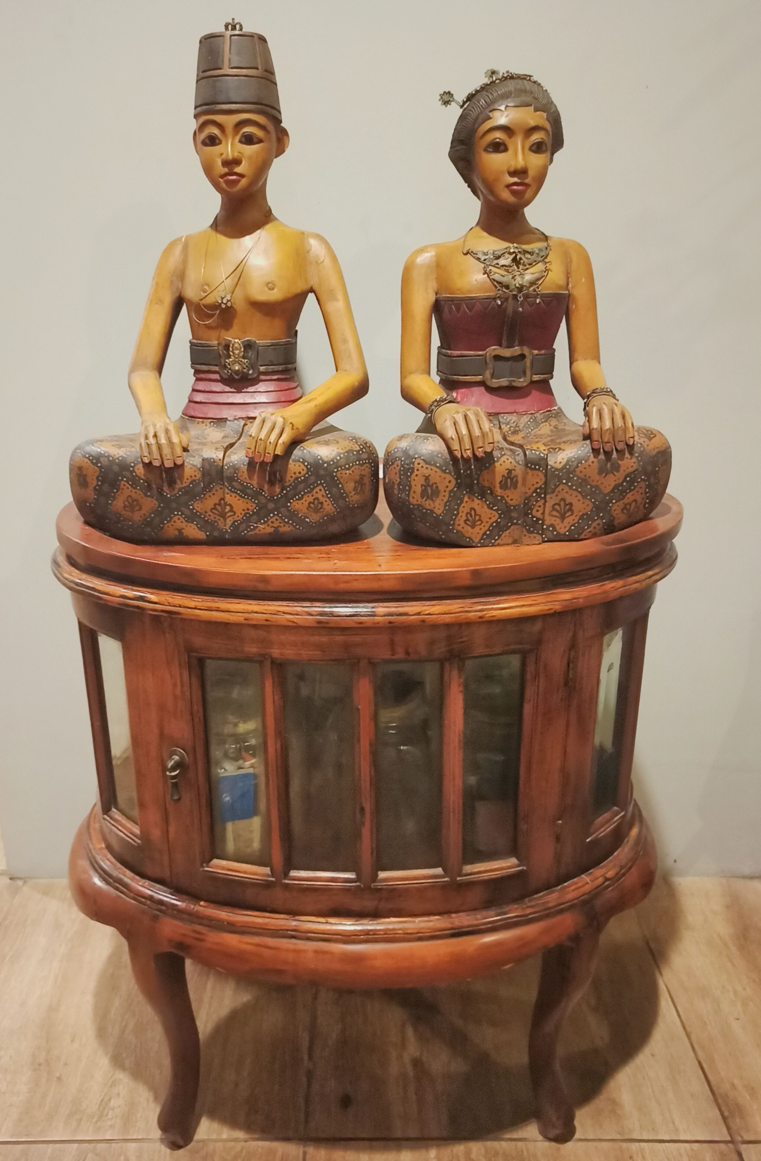 Two wooden statues with intricate designs on a round wooden table with glass panels.