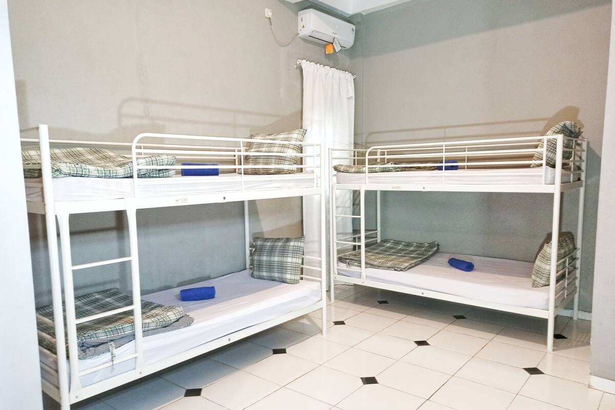 Une chambre avec deux lits superposés, chacun équipé d’un matelas et d’un oreiller, et un appareil de climatisation blanc fixé au mur.