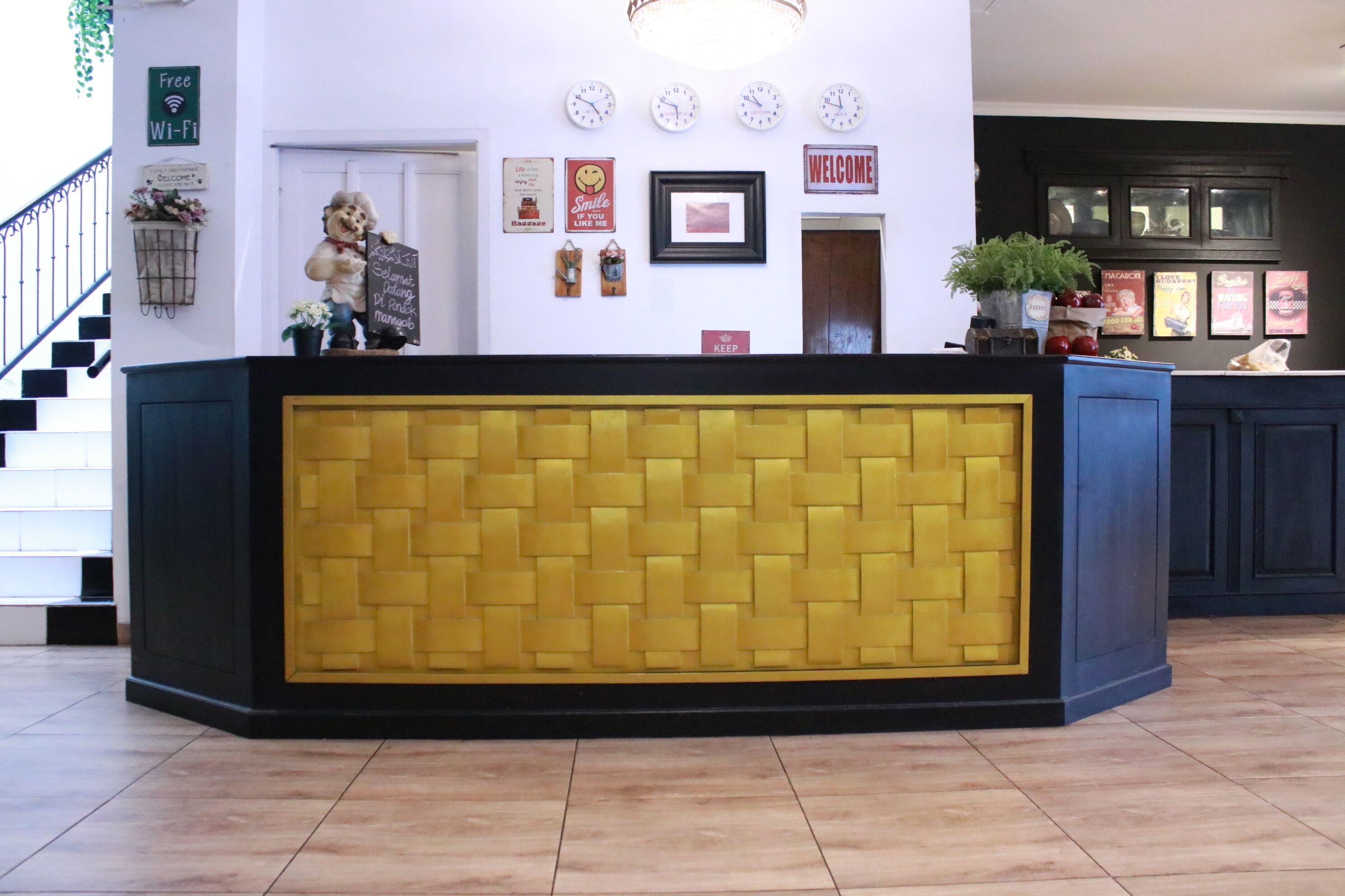 A reception area with a yellow and black reception desk, a staircase, and a wall decorated with clocks, signs, and a welcome sign.