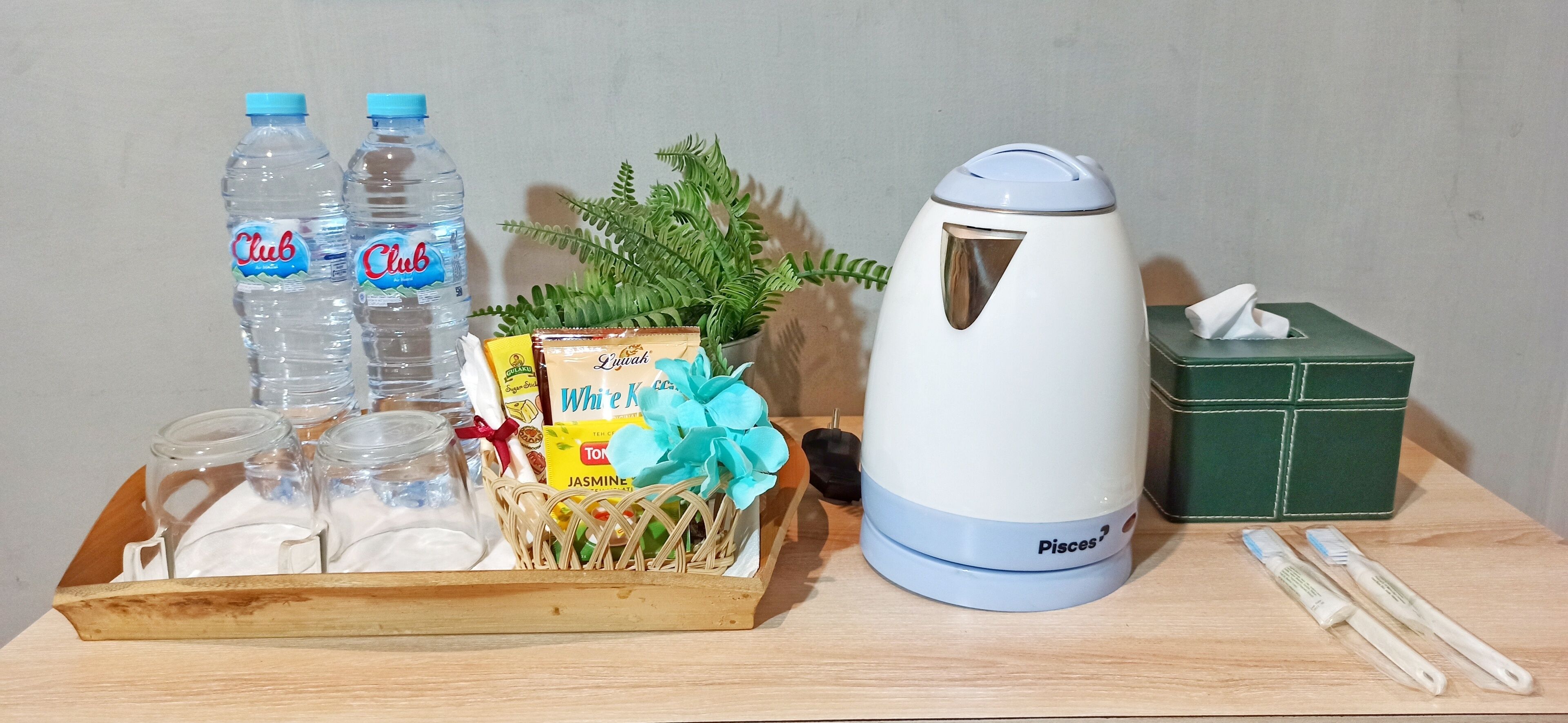 A wooden tray with Club water bottles, a jasmine tea box, a white kettle, a tissue box, and two toothbrushes.