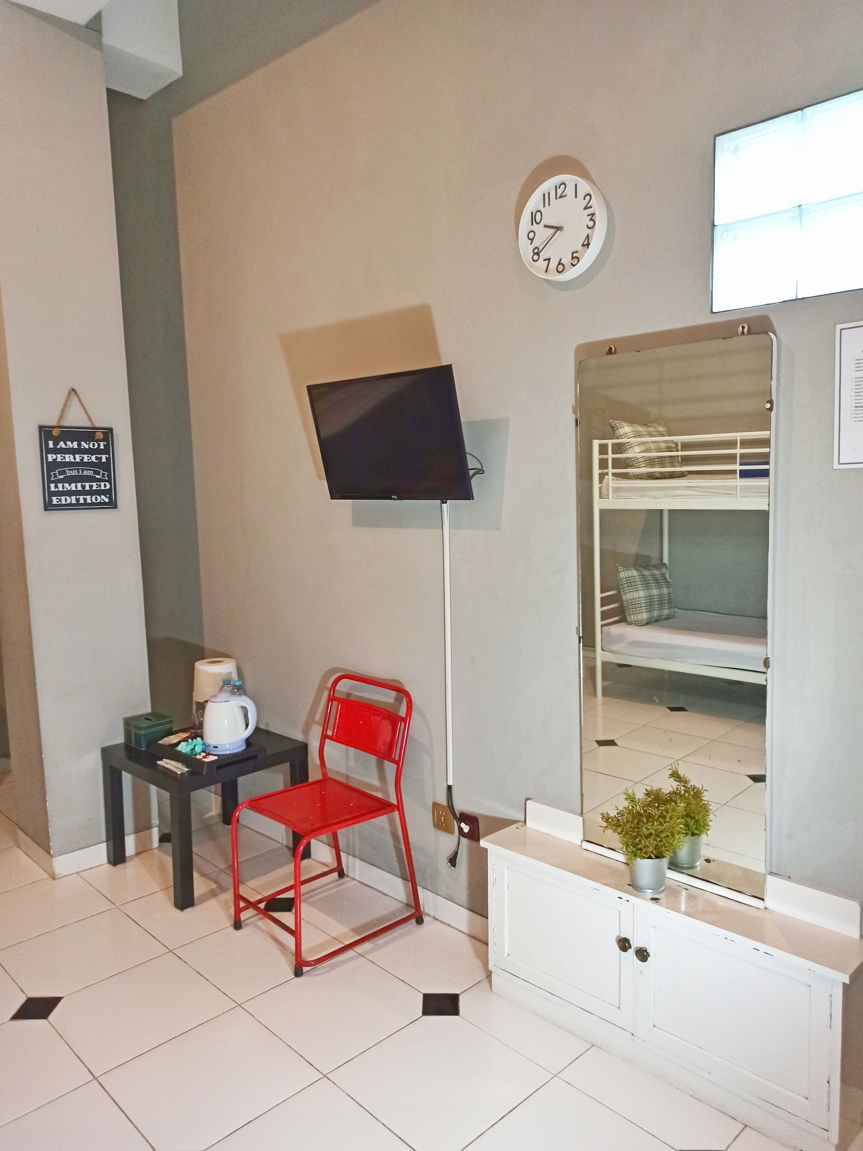 A room with a bunk bed, a desk with a chair, a television, a clock, and a sign on the wall.