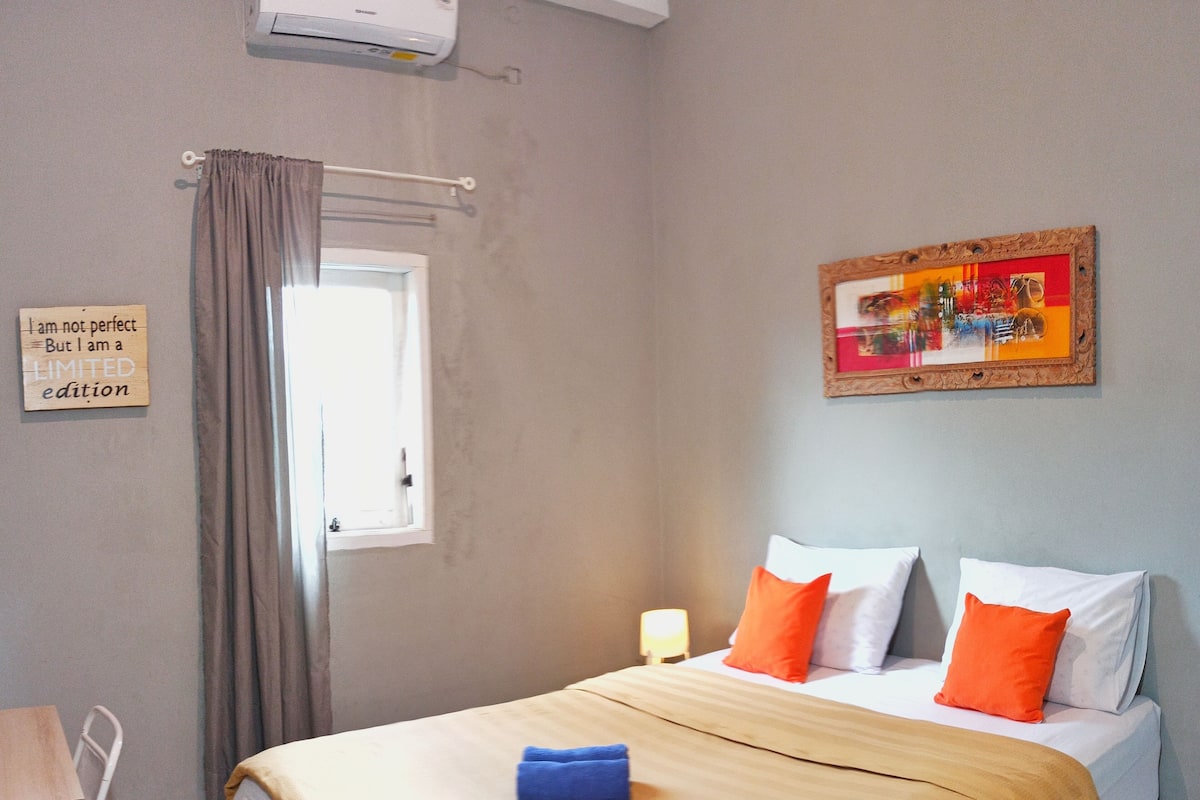 Une chambre d’hôtel avec un lit, une chaise, une table de chevet, un tableau et un panneau accroché au mur.