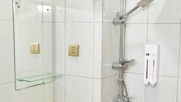 Une salle de bain avec un lavabo blanc, une étagère en verre, des toilettes et une douche équipée d’un pommeau de douche à main.