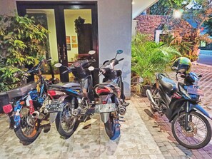 Three motorcycles parked in front of a building with a stone facade and potted plants.