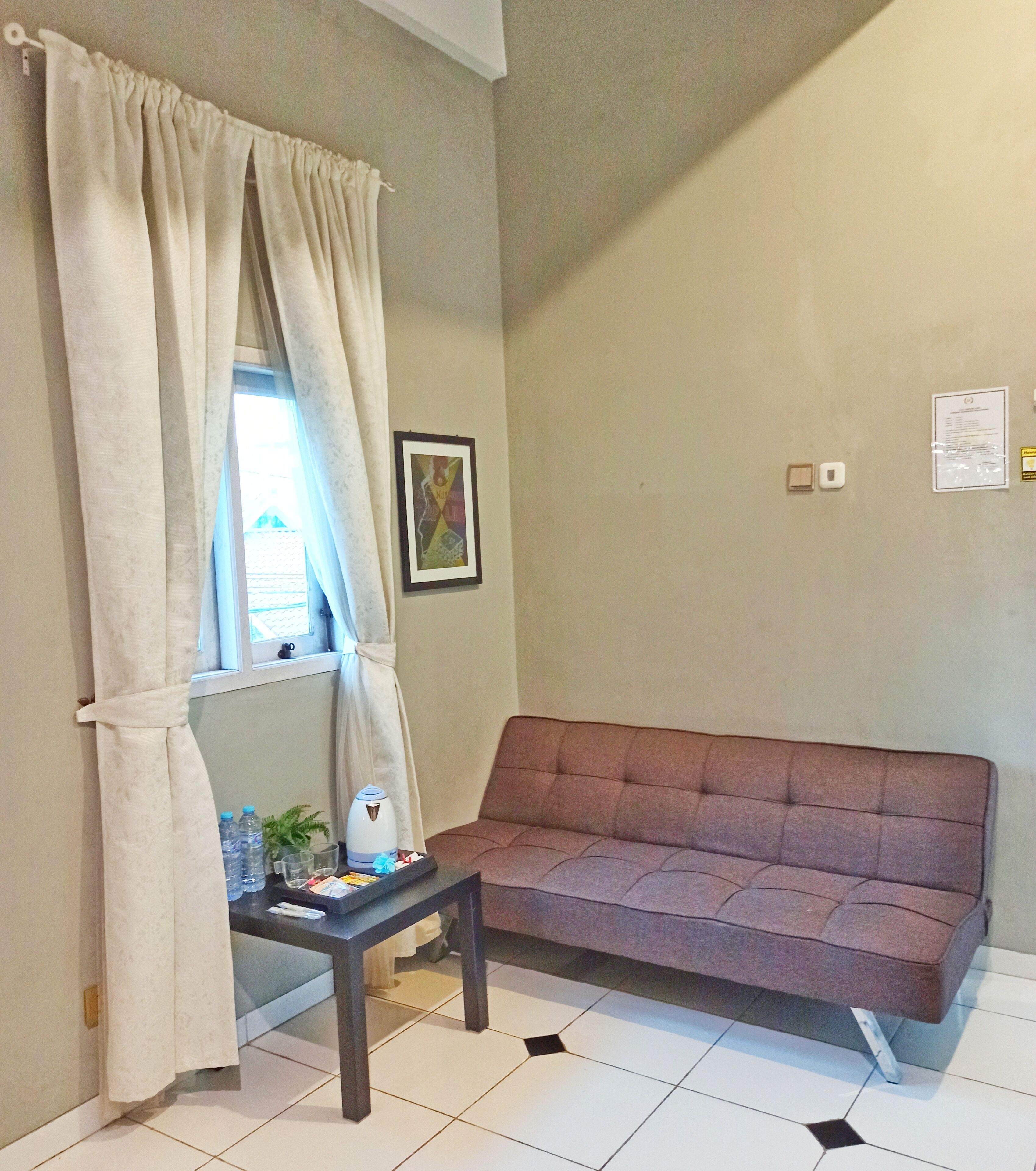 A room with a sofa, a small table with a kettle, and a window with curtains.