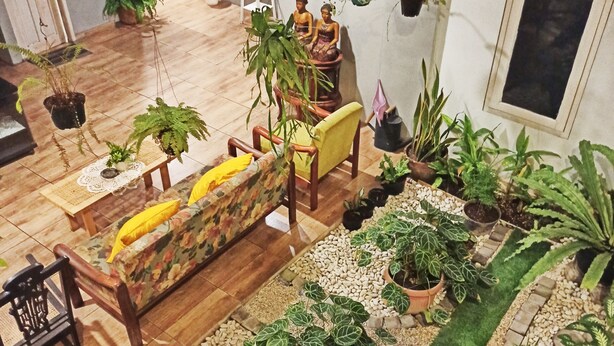 A spacious living area with a wooden sofa, chairs, and a variety of potted plants. - Manggolo Homestay Syariah (Yogyakarta)