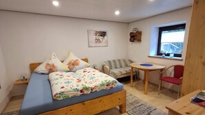 Een slaapkamer met een houten bed, een bureau, een stoel, een klein tafeltje, een raam en een wandplank.