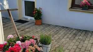 Een klein terras met plantenpotten en een houten bankje.