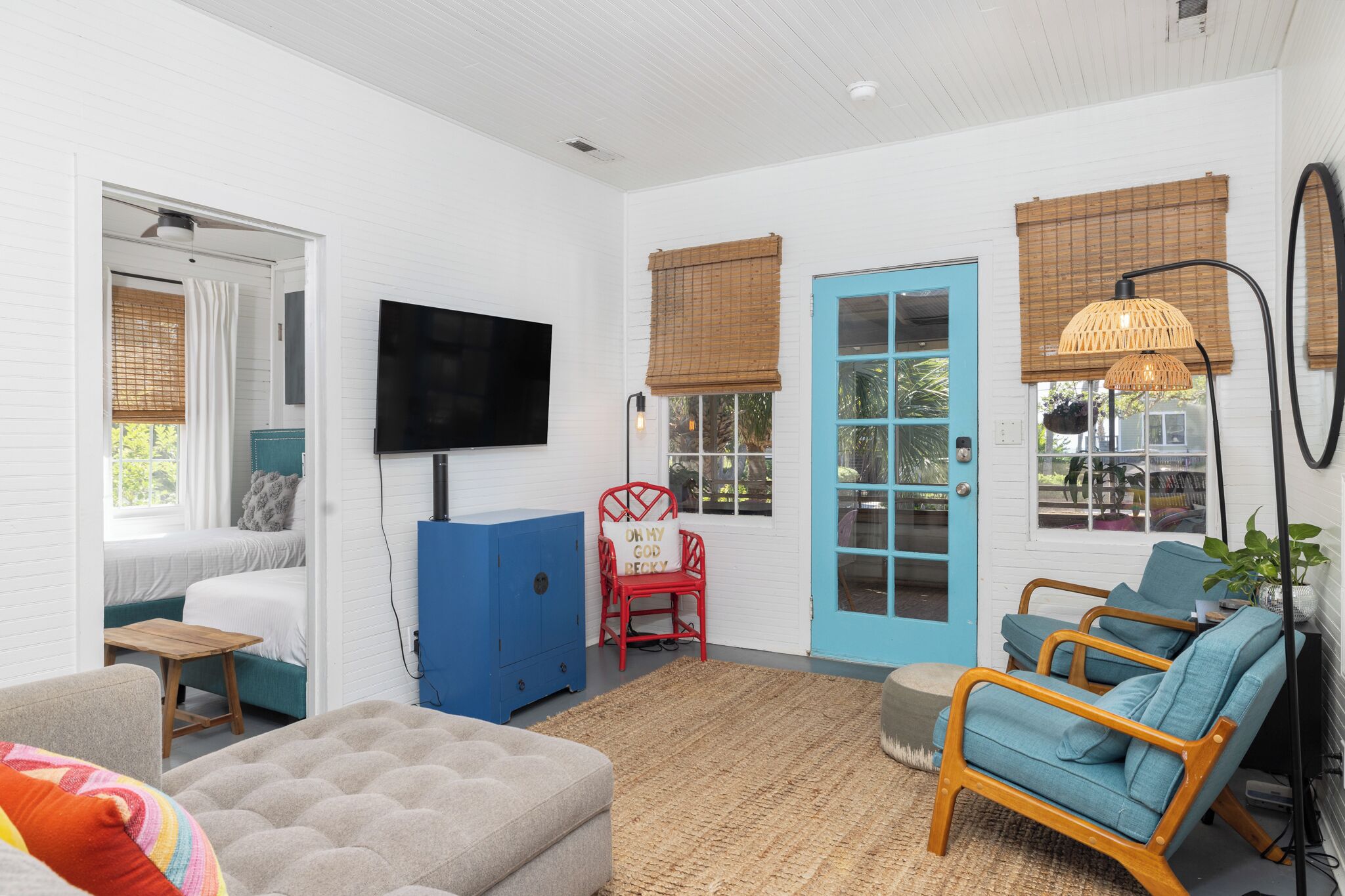 A room with a bed, a TV, a blue door, and a seating area with chairs and a rug.